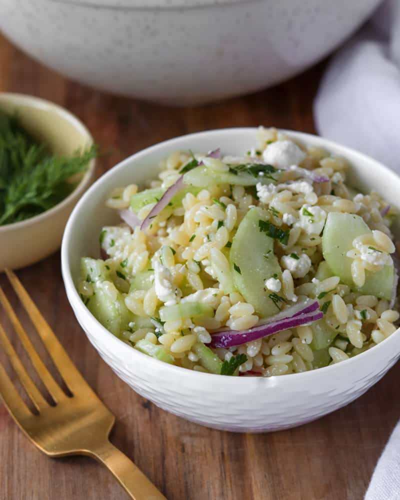 A small bowl of cucumber orzo pasta salad with red onions and feta cheese