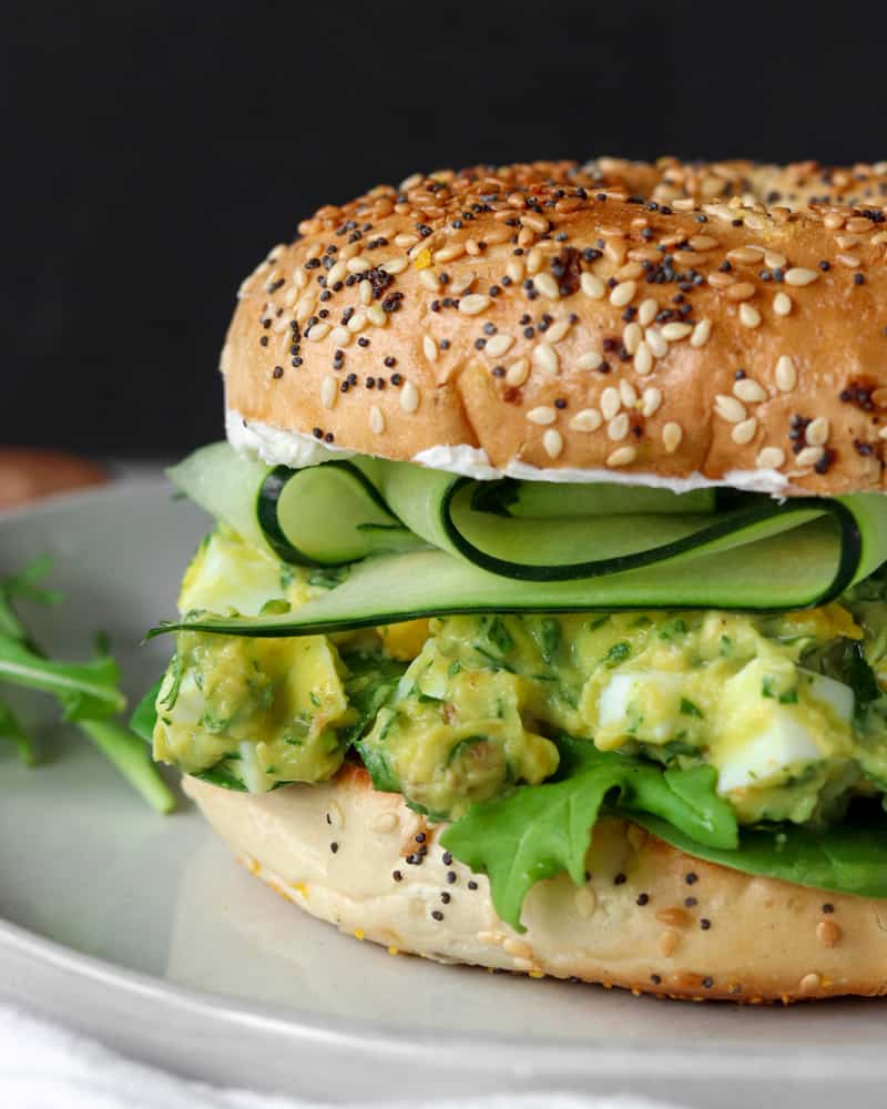 An everything bagel filled with greens, herby avocado egg salad, and cucumber ribbons
