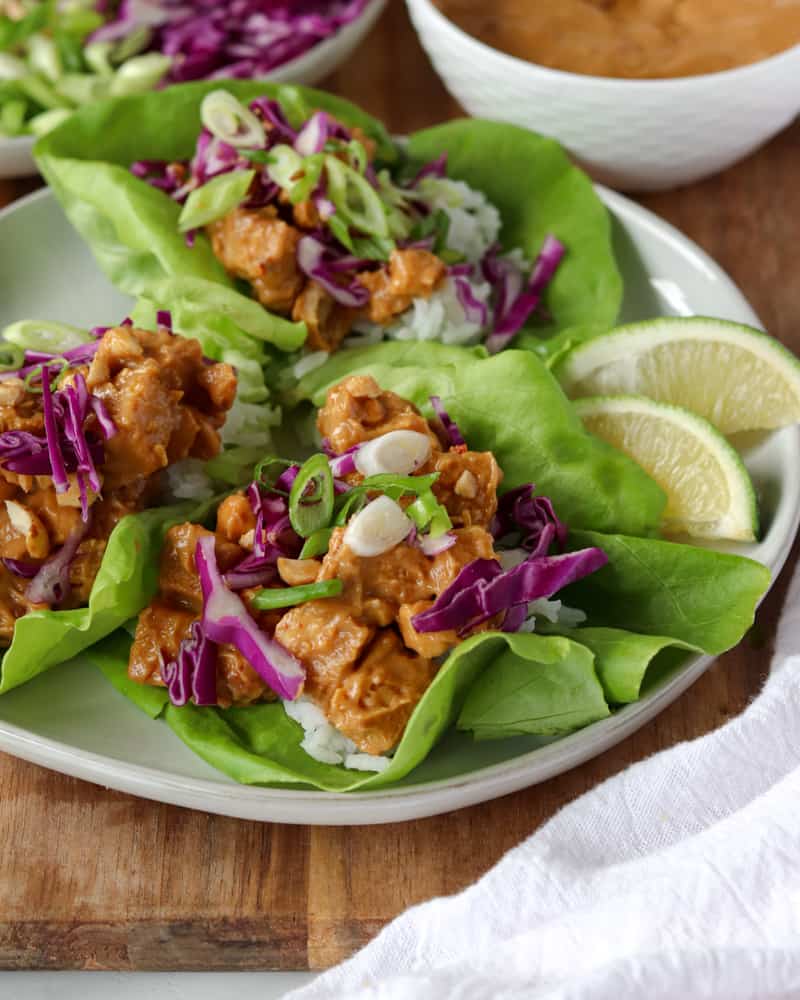Three colorful tofu lettuce wraps on a plate, with lime wedges on the side for squeezing on top