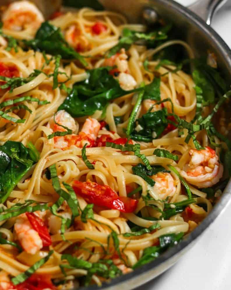 A pan full of linguine with tomatoes, shrimp and spinach in garlic butter white wine sauce