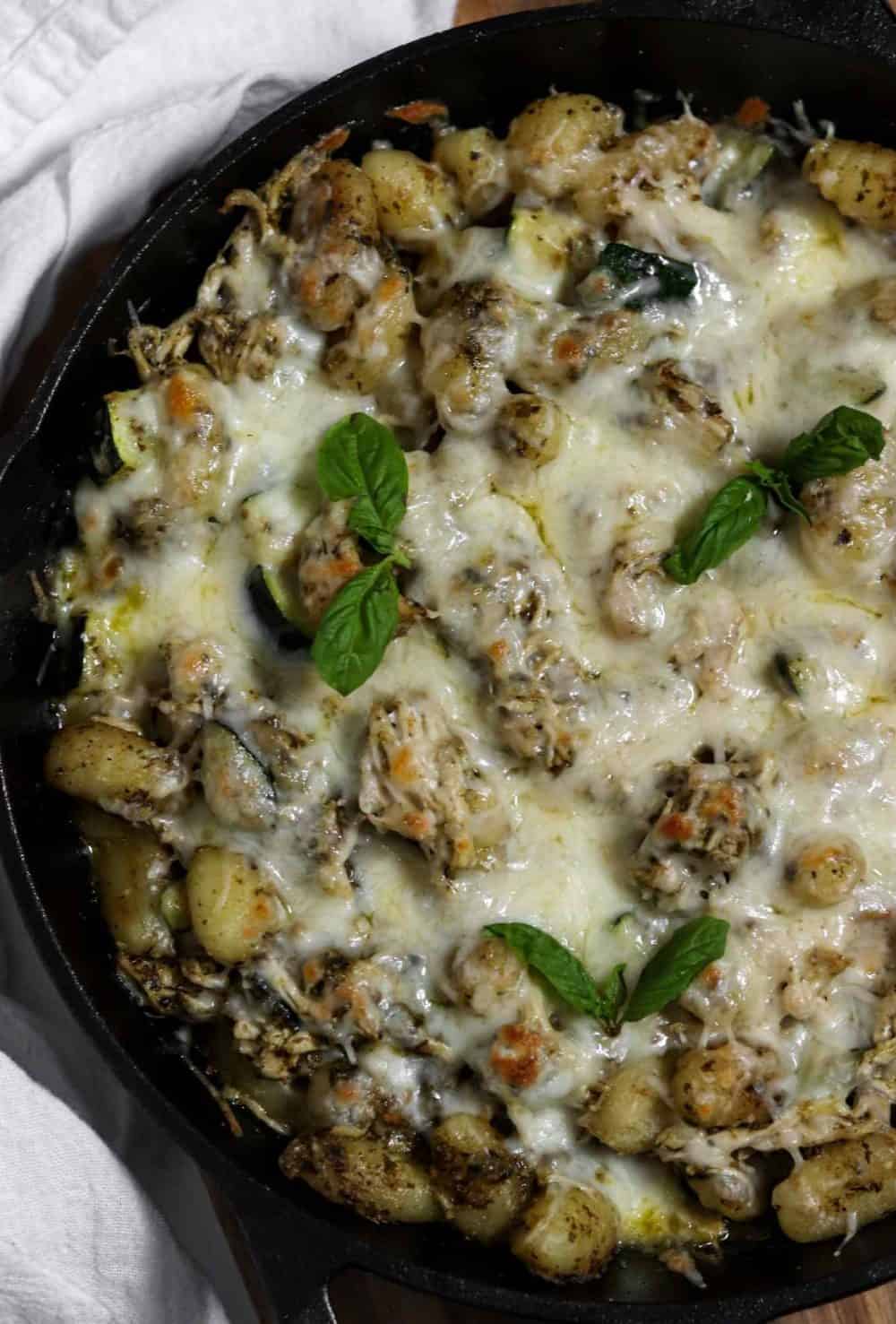 A cast-iron pan full of chicken and gnocchi tossed with pesto and topped with bubbly melted cheese