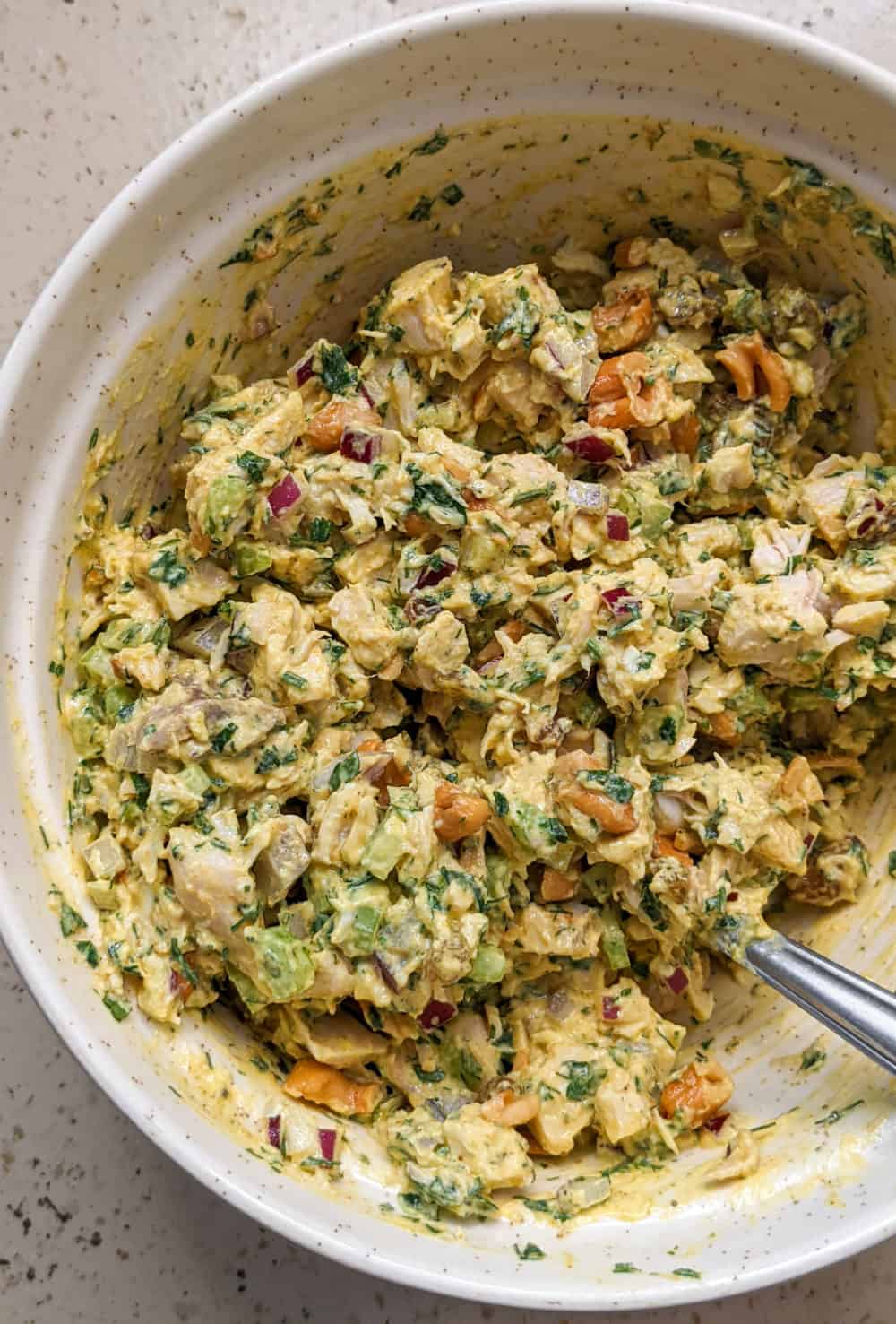 A bowl of curried chicken salad studded with chopped cashews, veggies, and lots of fresh herbs