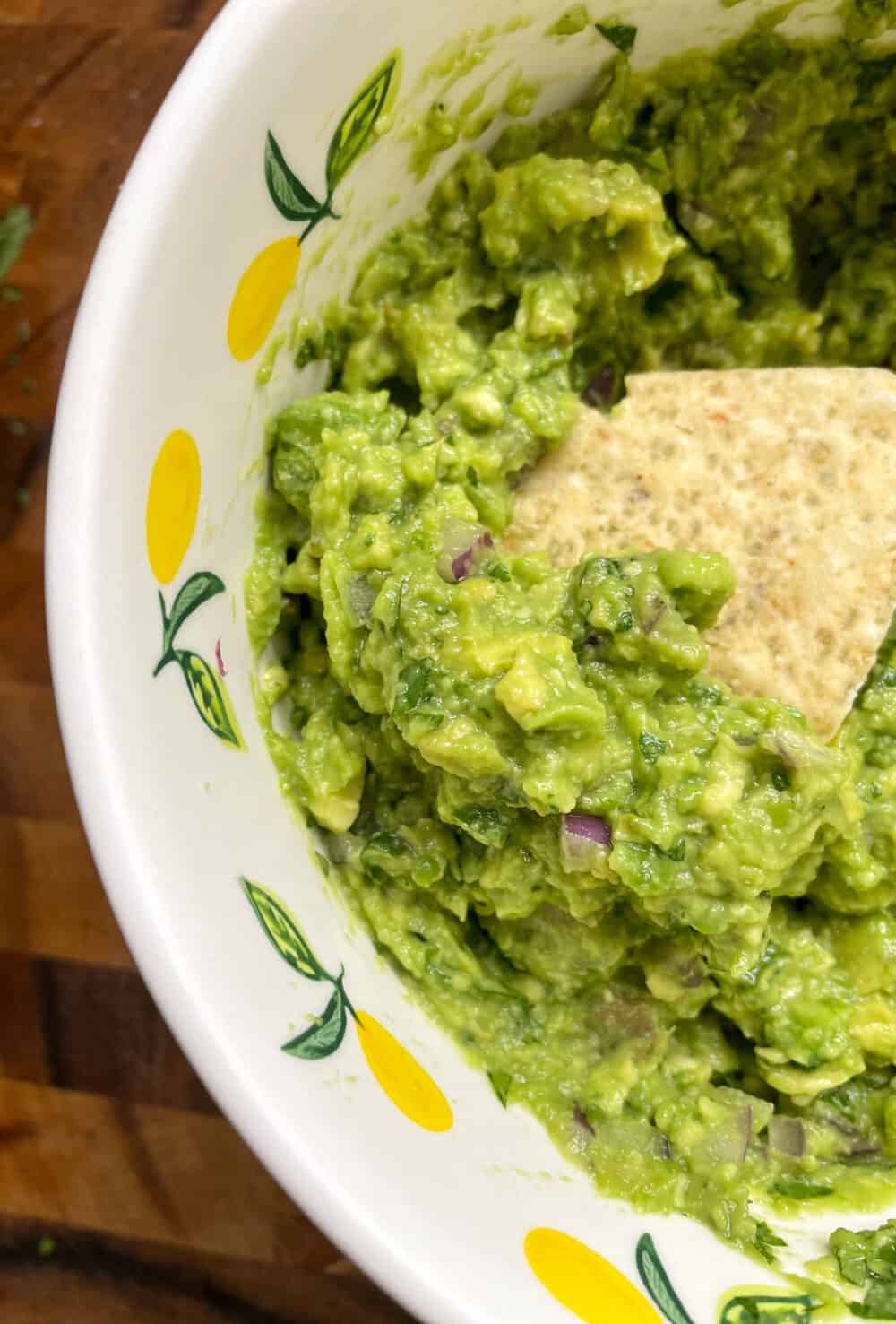 A bowl of chunky guacamole with a tortilla chip dipped in it