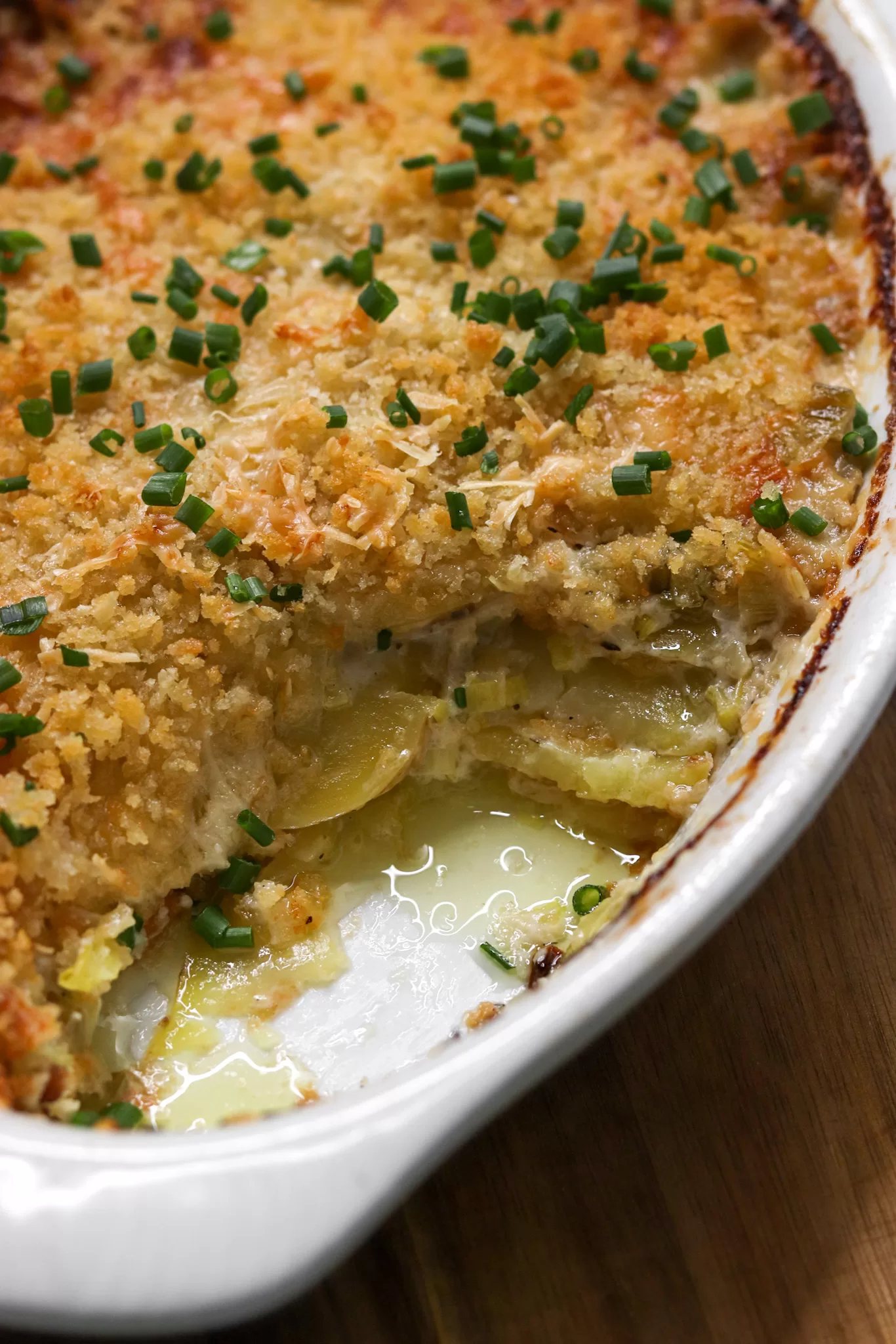 Potato leek gratin with a scoop taken out, showing the layers of thinly sliced potatoes inside.