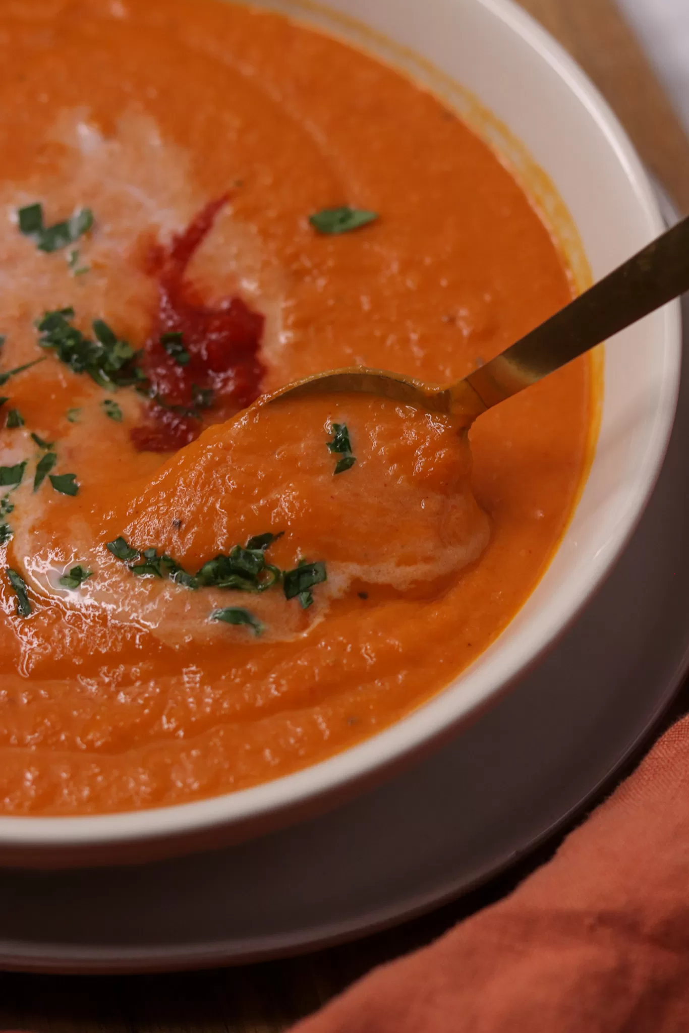 A spoon in a bowl of rich, creamy and vivid orange harissa roasted carrot soup.