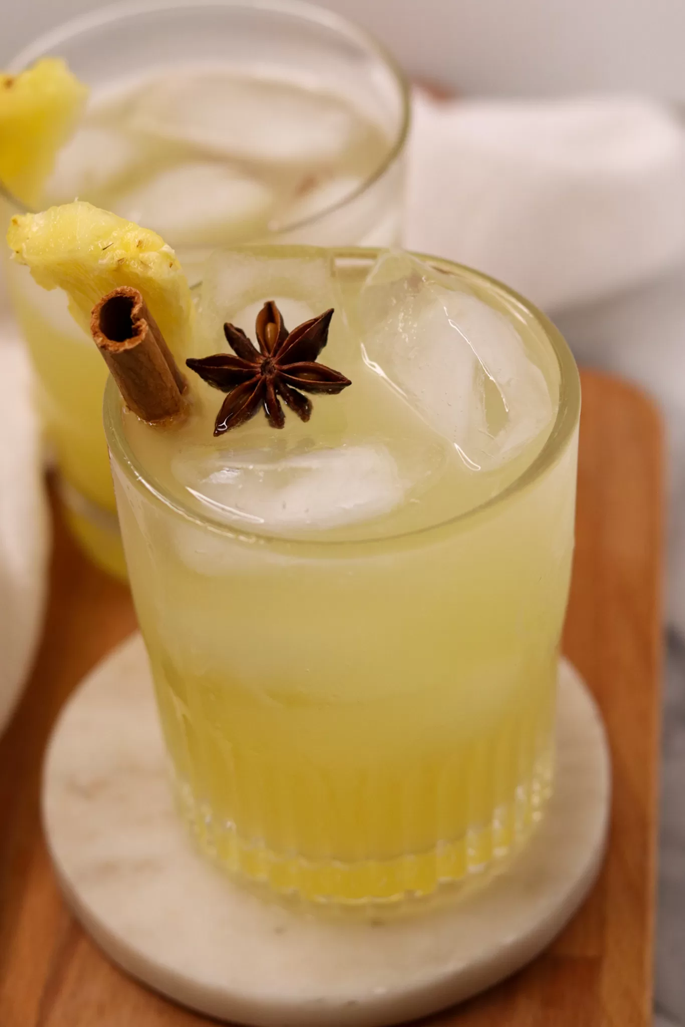 Yellow and bubbly pineapple ginger beer mocktail over ice in a rocks glass, garnished with star anise, a cinnamon stick and a pineapple wedge.