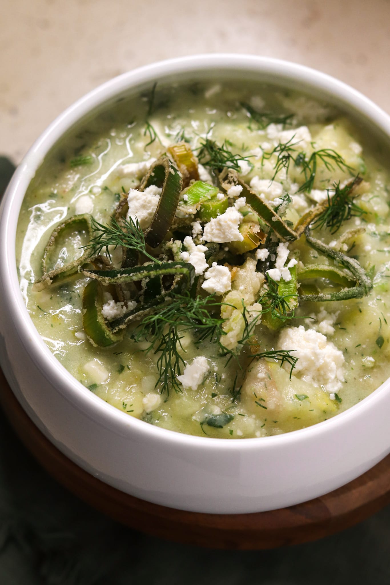 A close-up shot of a bowl of potato, leek and feta soup topped with crispy leeks, feta cheese and chopped dill.